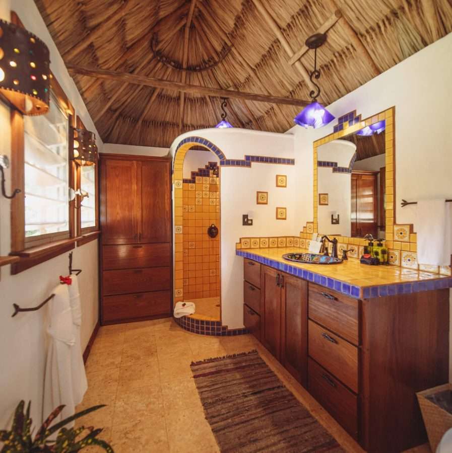 Bathroom with a hand-painted talavera tile walk-in shower, matching tiled double vanity, and a thatched conical ceiling.